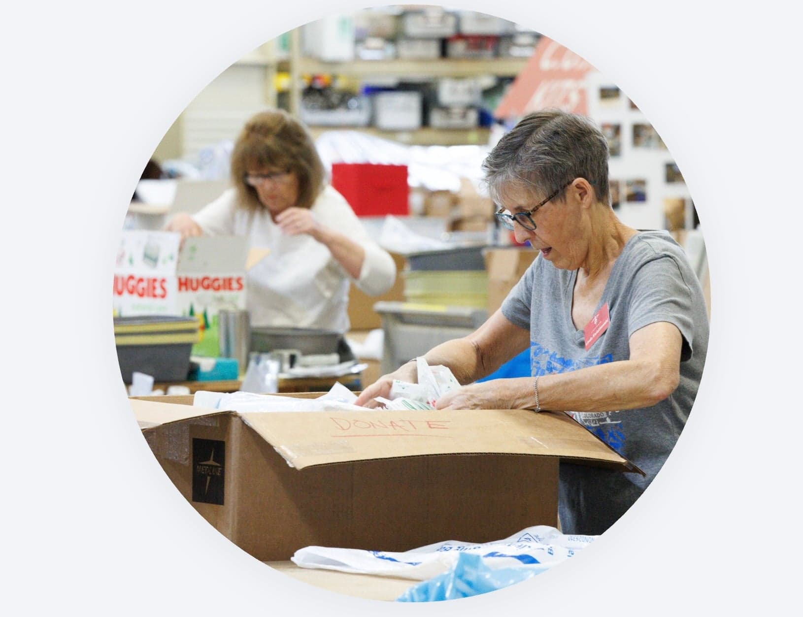 Two volunteers smiling while packing donation boxes with supplies.